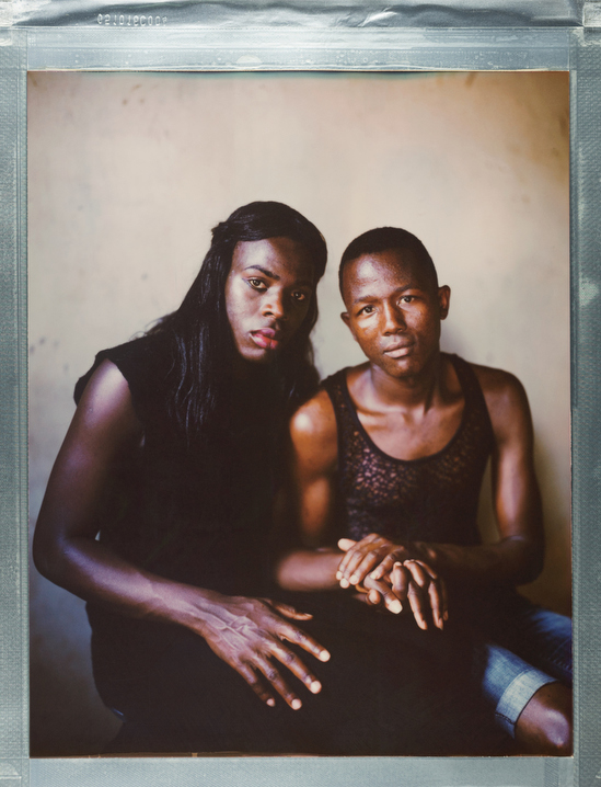 A posed portrait of 23 year old Ugandans Ashiraf (left) & Kajjan (right) in Nairobi. Ashiraf identifies as a transgender woman and Kajjan as gay. While same sex marriage is not legal in Uganda, in 2015 the pair conducted a marriage ceremony in a hotel to celebrate their relationship. “We had happiness at the party” says Ashiraf, and then adds “and that was the day.” That was the day their new married life began, and also the day their lives changed for the worse. A friend took photos of the wedding and posted them on social media. Local newspapers got hold of the photos and published them. Two weeks later their neighbors recognized them in the newspaper and went to the police. They locked their door when they heard the mob with the police coming, and hid inside. They could hear them trying to enter and talking together: “They said a lot of stuff, that we are sons of evil, we need to go to hell, we shall kill them direct if we get them.” That night they packed their bags and left for Kenya. But life in Kenya was not what they had hoped. They struggled to be registered by the United Nations refugee agency, and struggled even more to find a place to settle down: “After three months in Kenya, our life was not good at all, as we kept on migrating from one place to another because Kenya is like Uganda they don’t allow us in here. We were beaten, abused, tortured on the way when we were moving,” says Ashiraf. “My boyfriend is HIV positive and I am negative but I have (high blood) pressure. Life is hard because we don’t have money to eat yet we have to take our medicine. The landlord is chasing us out of the house because we don’t have money. I tried to look for jobs but couldn’t get because I naturally look like a transgender. Whenever I go to look for jobs I am abused that I am a lady, sometimes beaten.” Kajjan reiterates the sentiments expressed by his wife: “Up to present time, we are still suffering because I am HIV positive though my boyfriend isn’t, we have nothing to eat, nor food.” Kenya, October 2017.
Nature Network is a Nairobi based organization providing LGBTQI+ refugees in Kenya with support through safe temporary housing, health services, food and security. Nature Network has advocated to police over 50 times, responding to hate crimes, and runs a WhatsApp group of safety tips. Refugees supported have come from Uganda, Somalia, Burundi, Rwanda and Sudan. 
While in many places, there has been great progress in recent years in the movement for lesbian, gay, bisexual, transgender, or intersex (LGBTQI+) rights, including an increasing recognition of same-sex marriage, nearly 2.8 billion people live in countries where identifying as LGBTI is subject to rampant discrimination, criminalization, and even death. Same-sex acts are illegal in 76 countries; in some countries, this can result in being sentenced to death. Behind these statistics, there individuals with unique, often harrowing stories. Where Love Is Illegal was created to tell those stories. 
Robin Hammond/NOOR for Witness Change
